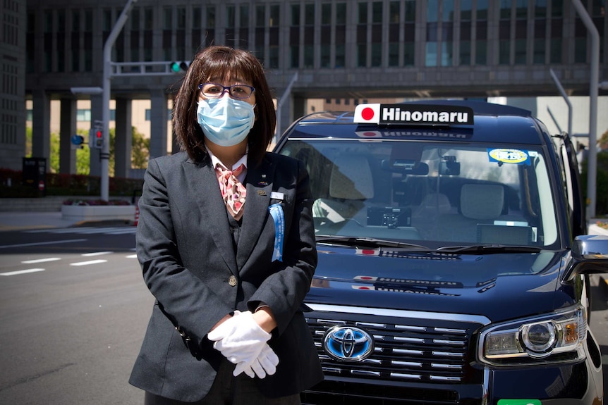 A woman standing in front of a taxi wearing a face mask