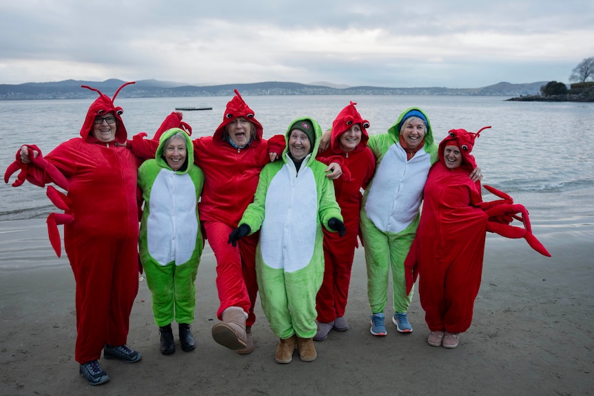 Ladies dressed in lobster and frog costumes standing at a beach, smiling.