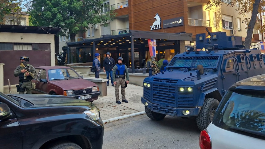 Armoured police stand next to a military-style transport vehicle in a town centre.