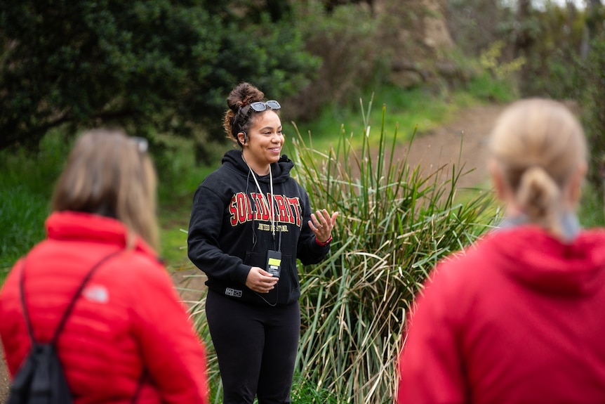 Aboriginal woman smiling with sunglasses on head addresses two walkers on a walking track 