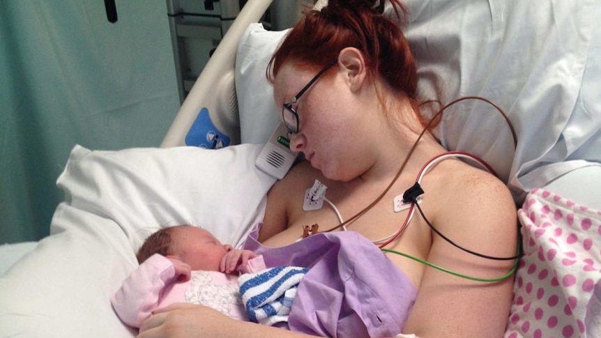 Jessica Linwood lies in a hospital bed looking at her baby daughter Harper, with wires attached to her shoulders monitoring her