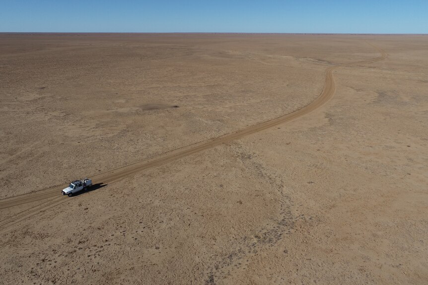 An aerial shot of a ute driving through an arid landscape.