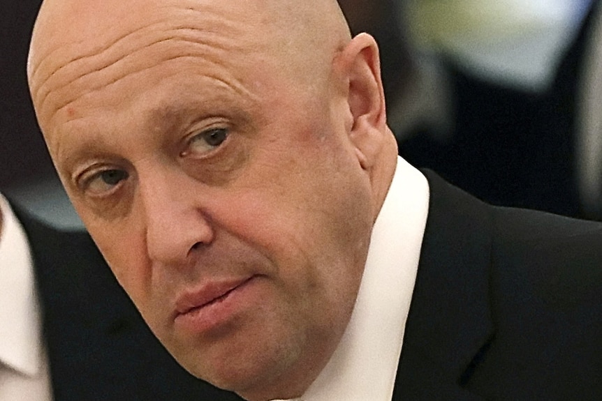 A close up of Yevgeny Prigozhin dressed in a black suit as he looks over his shoulder.
