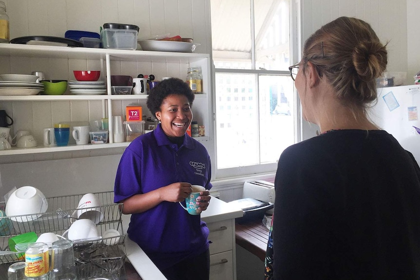 Miriel (last name withheld), now 19, smiles in a kitchen with another woman in a house in Brisbane