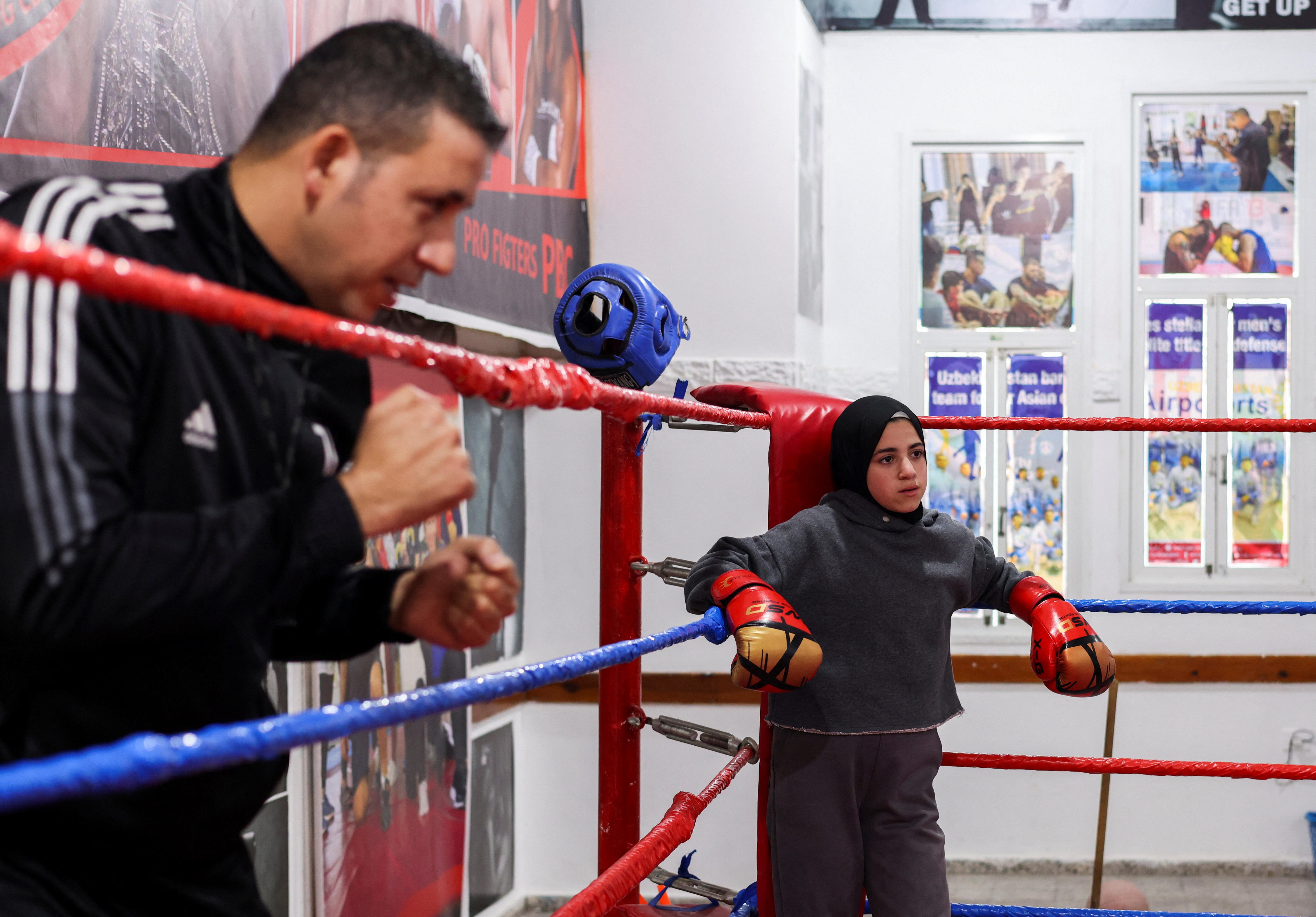 A girl leans against the edge of a boxing ring as a man watches. 