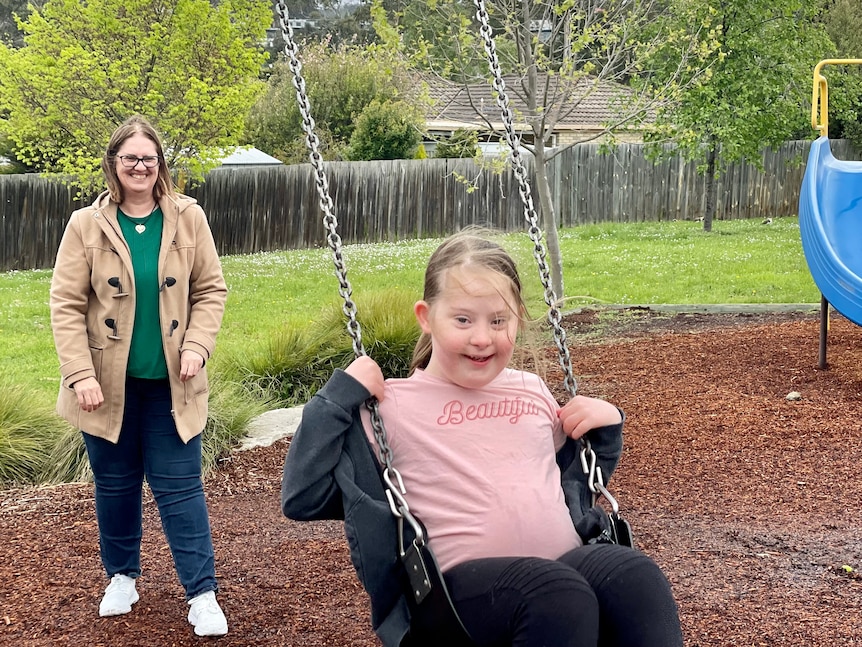 A woman pushes a child on an outside swing