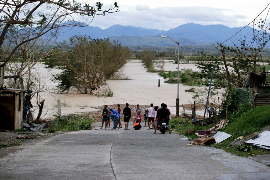 Wide shot of a group of people standing on a flooded road.