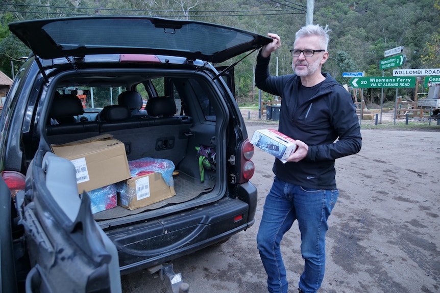 A man holds a UHF radio inside packaging next to a car with boxes in the boot.