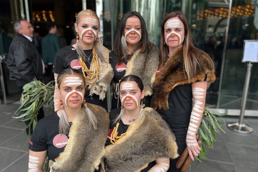 Aboriginal women, dressed in possum-skin cloaks, stand together.