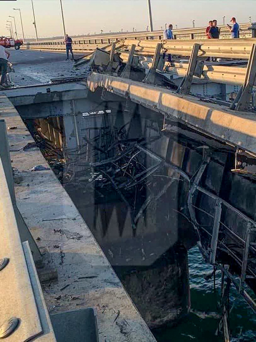 People standing around the damaged section of a bridge