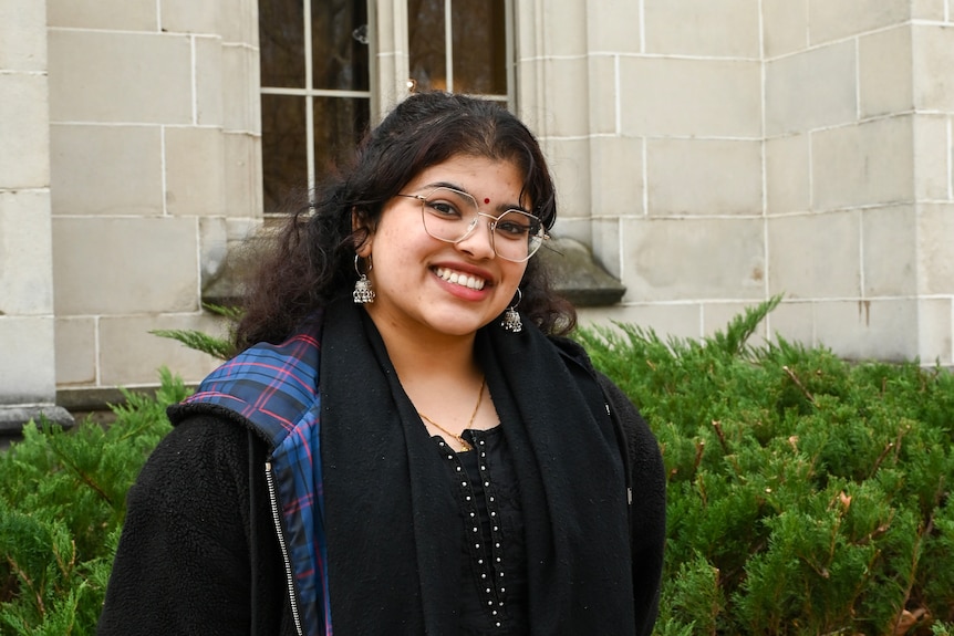 Arati, a psychology student at her university campus. She is dressed in black and is wearing glasses.