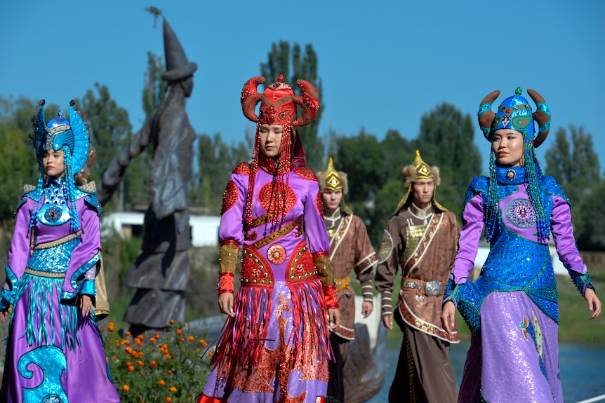 Members of the Russian folk dance ensemble from Adygea walk in a line, dressed in colorful clothes. 