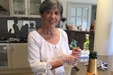 Doreen Collyer stands at a kitchen bench with a bottle of champagne and two glasses in front of her.
