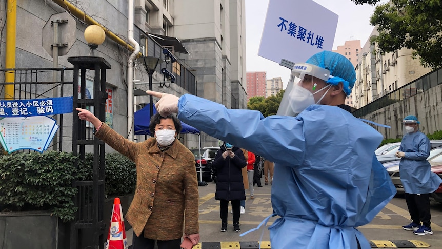 A worker in a hazmat suit points and older woman to the left of frame.
