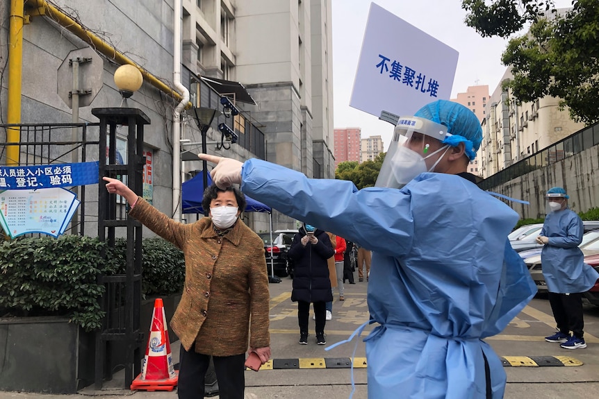 A worker in a hazmat suit points and older woman to the left of frame.