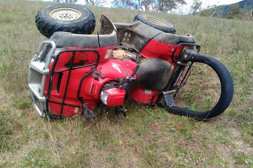 A quad bike with roll over protection bar lying on its side in a paddock.