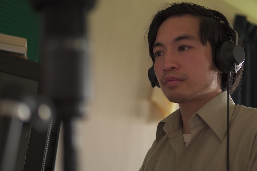 Asian man wearing headphones looking at a computer screen.