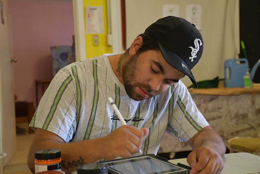 A young man in a hat and striped shirt uses an E-pencil to make art designs.