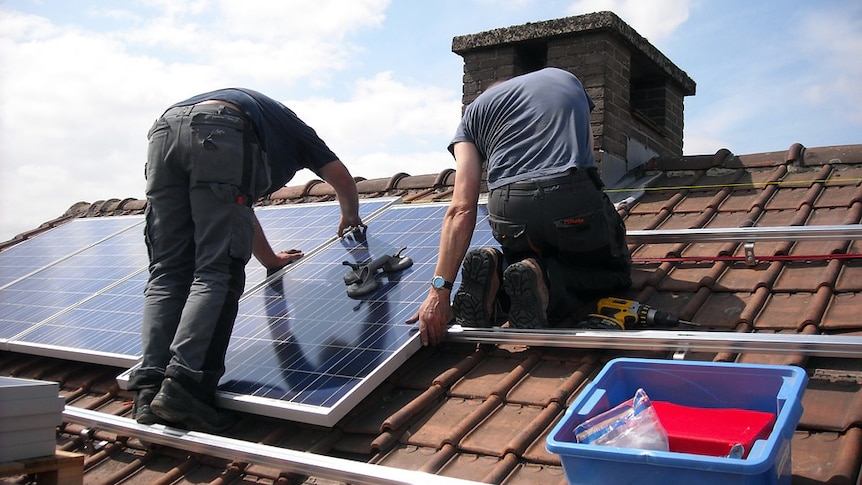 Two men install solar panels on the roof of a house.