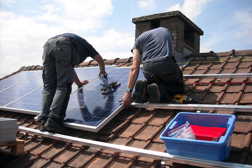 Two men install solar panels on the roof of a house.