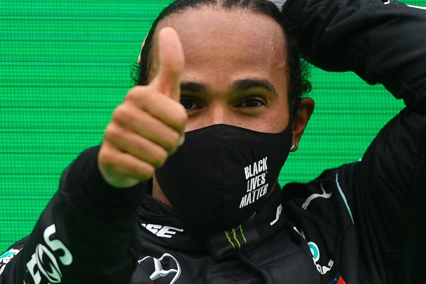 Lewis Hamilton gives a thumbs up while wearing a face mask that reads BLACK LIVES MATTER
