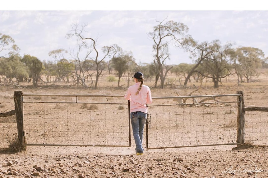A girl opens a gate, surrounded by dry farmland