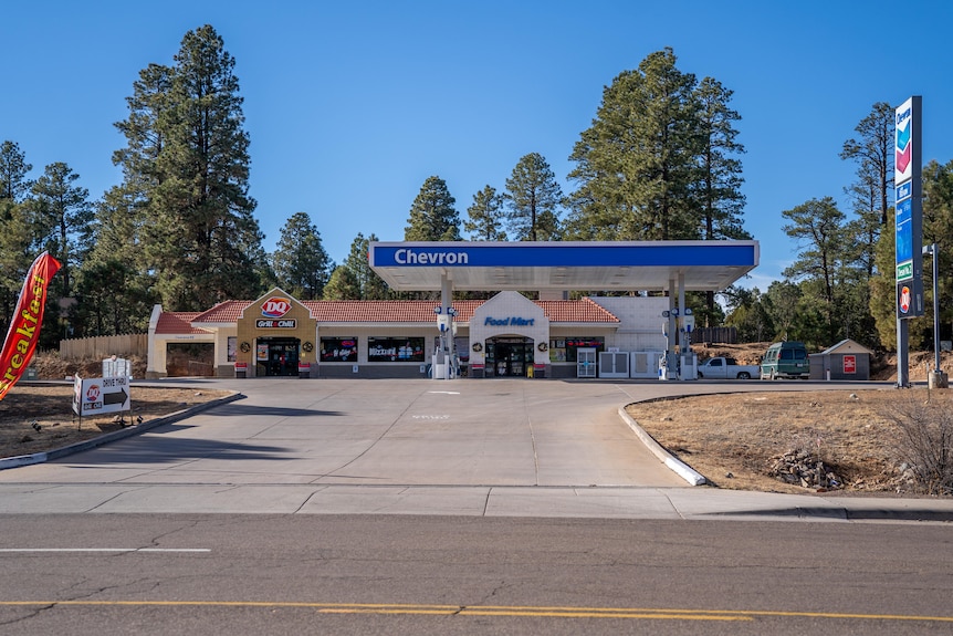 The entrance to the parking area of a gas station with blue signage seen from across the road
