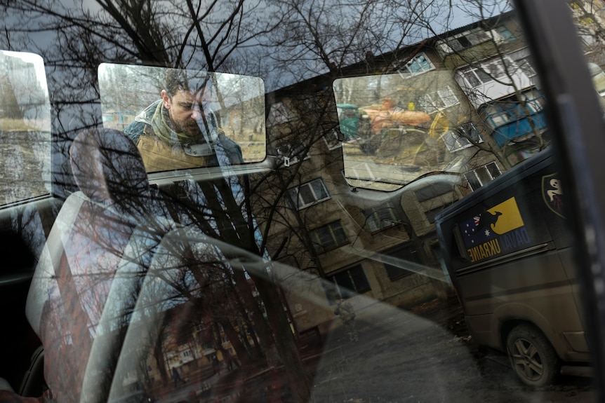 Apartment blocks reflected in the windows of a 4WD, with a man peering in
