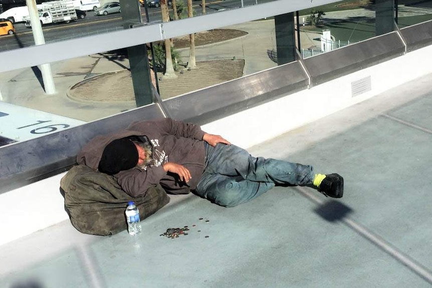 Homeless man lies asleep on a street of LA