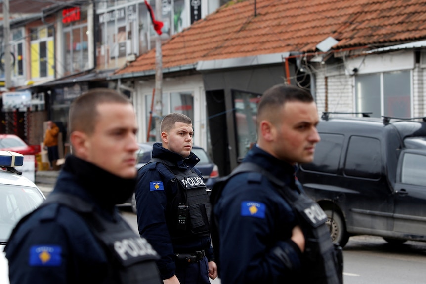 Trei ofițeri de poliție din Kosovo în uniformă stau pe o stradă