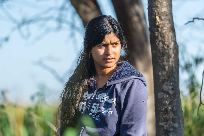 A woman wearing a tracksuit top stands in the middle of bushland.