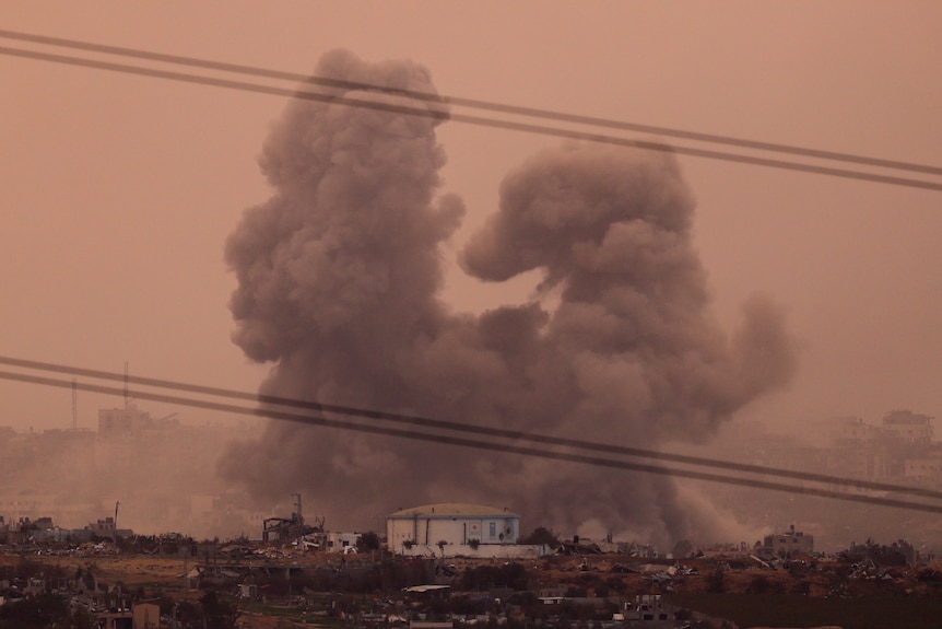 An orangish pink sky as a large smoke cloud is seen above Gaza 