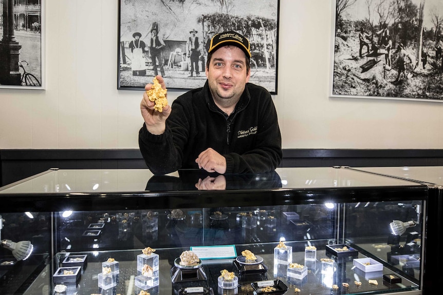 A man holding a gold nugget in front of a shop counter.