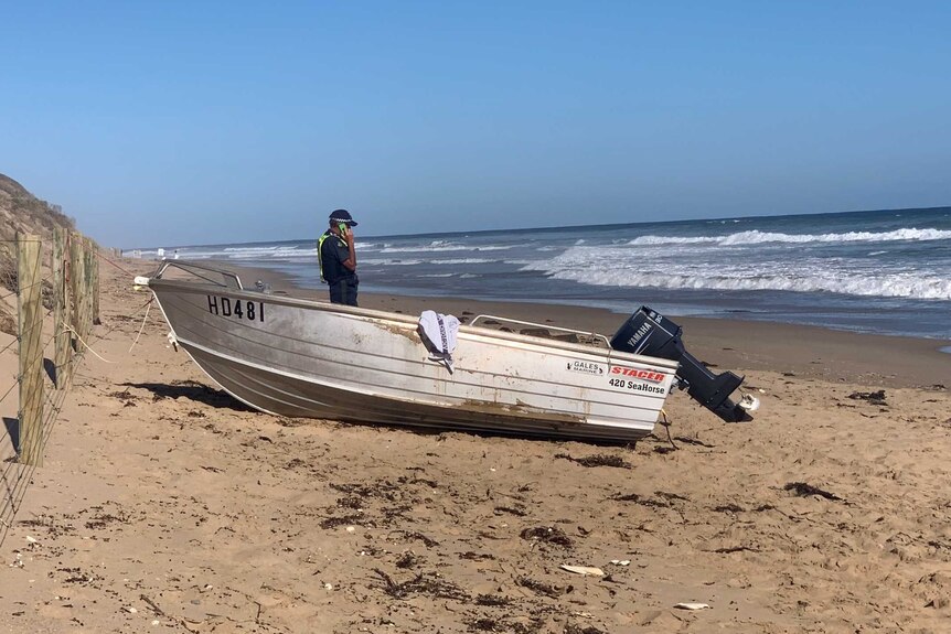 A police officer stands next to a boat on the beach at Anglesea.