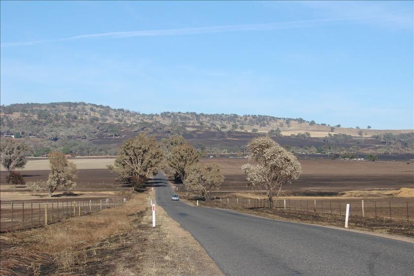 A long road with scorched paddocks littered on either side.