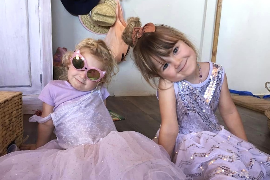 Two smiley girls in purple ballet dresses smiling at camera, one with sunglasses
