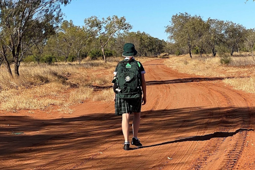 A student, in uniform, walks along a dirt track