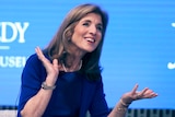 Caroline Kennedy smiling and gesturing against a blue background.