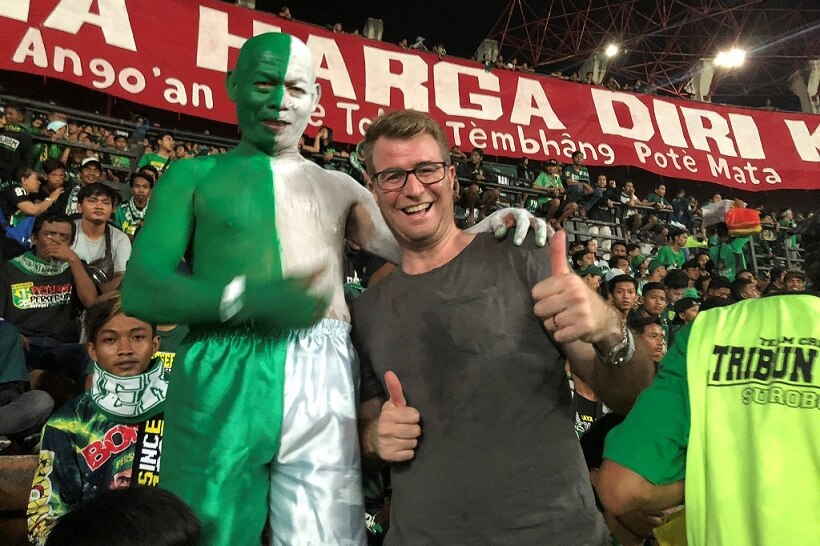 David Lipson poses with a fan painted half green and half white, at a soccer match in Indonesia.