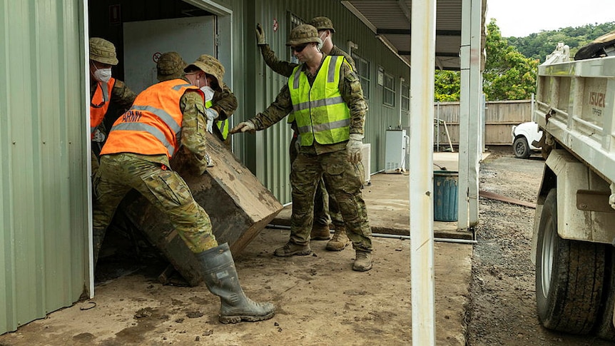 Soldiers in uniform clearing damaged furniture from a shed.