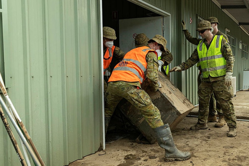 Soldiers in uniform clearing damaged furniture from a shed 