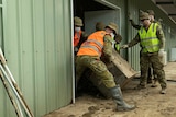 Soldiers in uniform clearing damaged furniture from a shed.