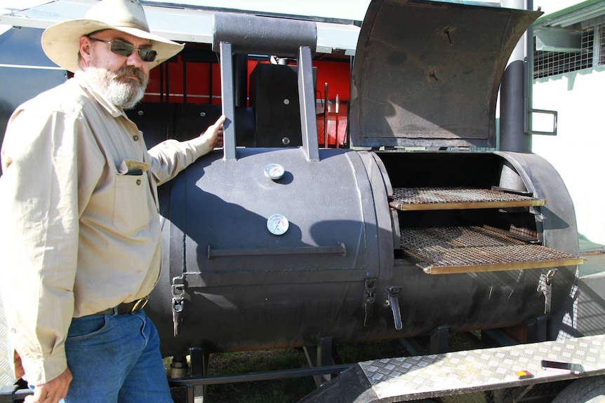 Matthew Noakes stands beside mobile wood-fired bbq.