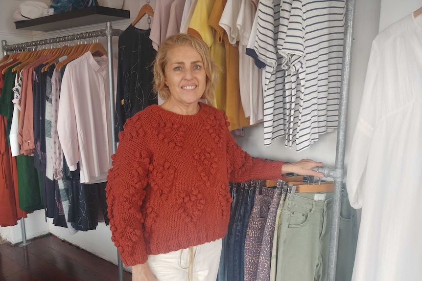 A woman stands infront of a clothes rack.