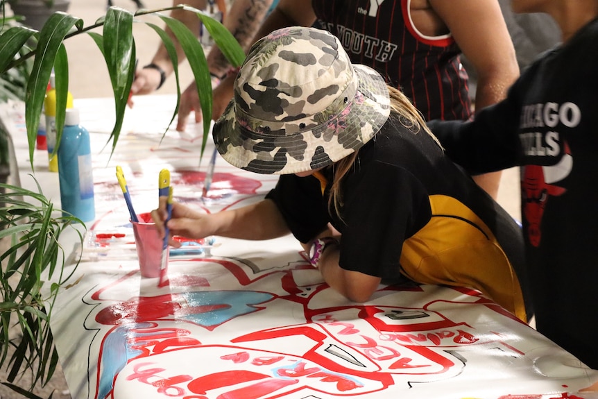 A youth draws on paper with red texta.