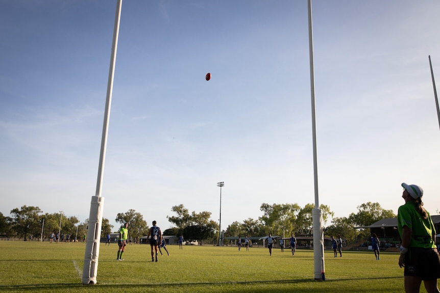 Un ballon de football de l'AFL s'élève dans les airs vers deux poteaux de but blancs.