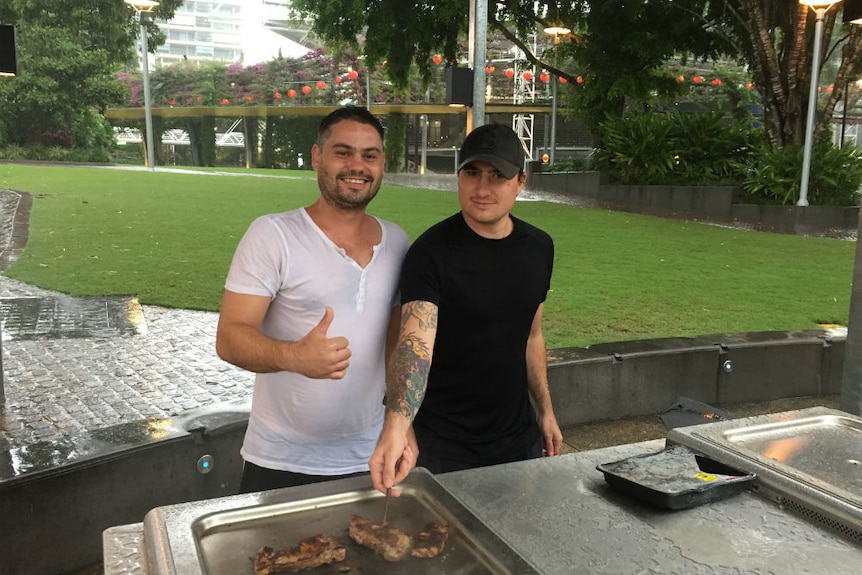 Two men look enthusiastic as they barbeque some steaks in South Bank, Queensland, using a stick as makeshift "tongs".