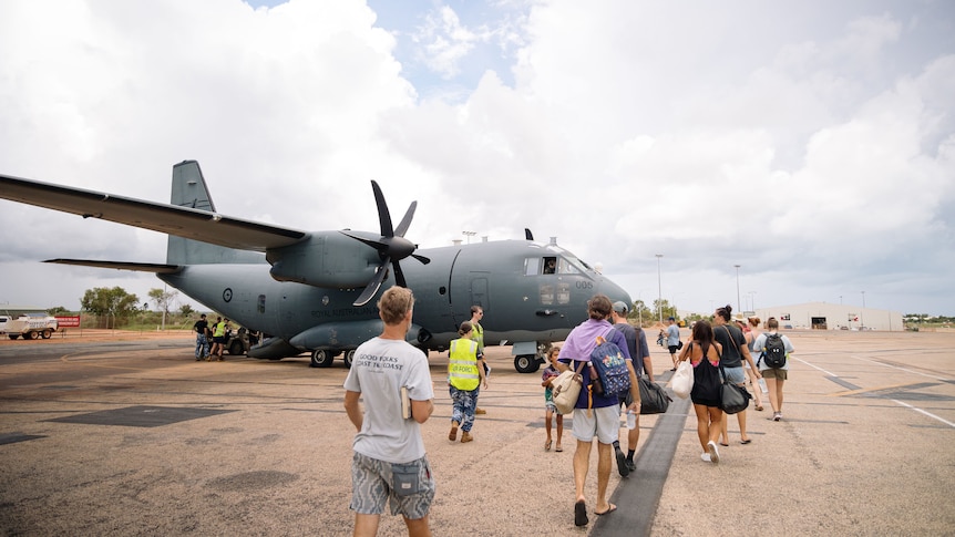 A group of civilians walking towards a large military plane on airstrip.