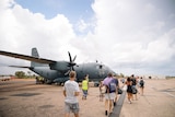 A group of civilians walking towards a large military plane on airstrip.