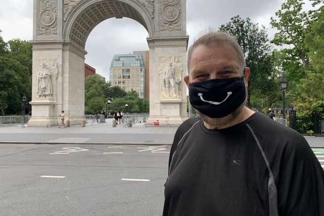 Paul Gauger wearing a black mask with a white smile on it, standing outside Central Park in New York